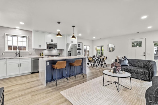 interior space featuring a kitchen island, pendant lighting, sink, white cabinetry, and appliances with stainless steel finishes