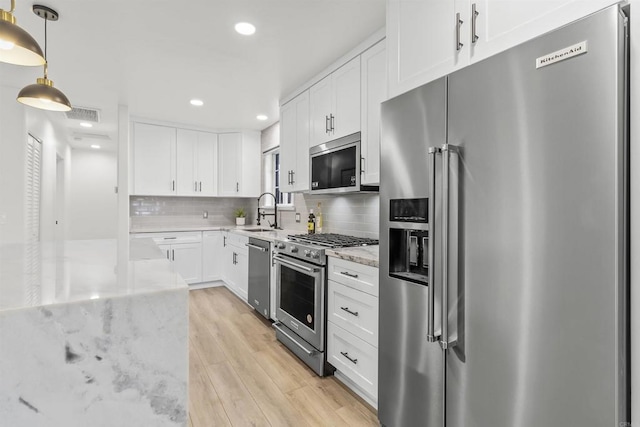 kitchen with tasteful backsplash, sink, hanging light fixtures, stainless steel appliances, and white cabinets