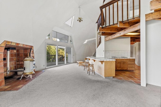 kitchen with a high ceiling, a kitchen bar, a wood stove, ceiling fan, and light colored carpet