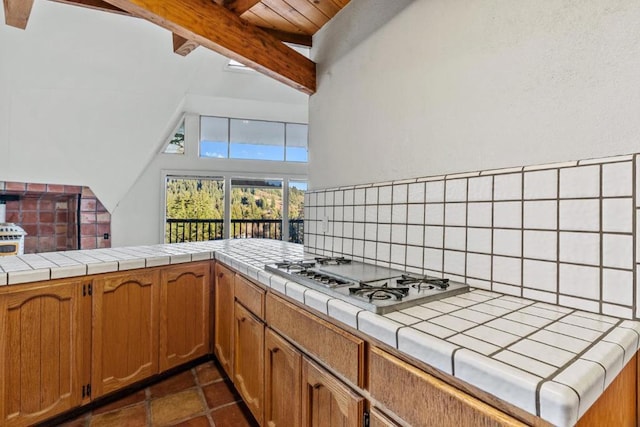 kitchen with kitchen peninsula, stainless steel gas stovetop, tile counters, and tasteful backsplash