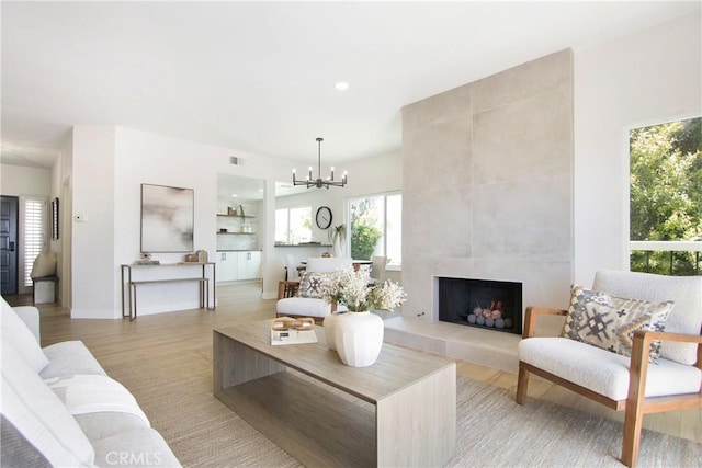 living room with a tile fireplace, a chandelier, and light hardwood / wood-style flooring