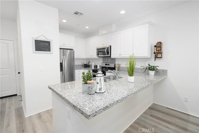 kitchen featuring kitchen peninsula, stainless steel appliances, light stone countertops, white cabinets, and sink