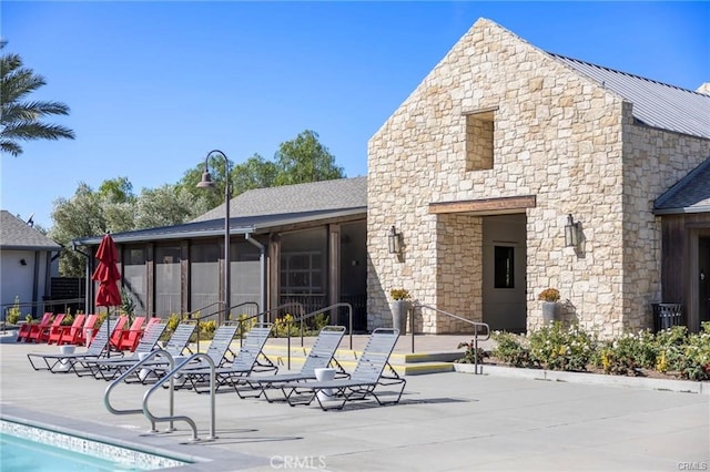 back of property featuring a community pool, a patio area, and a sunroom