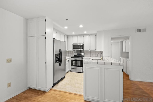 kitchen with white cabinets, appliances with stainless steel finishes, sink, kitchen peninsula, and light wood-type flooring