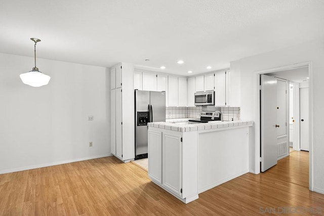 kitchen featuring appliances with stainless steel finishes, kitchen peninsula, tile counters, and white cabinetry