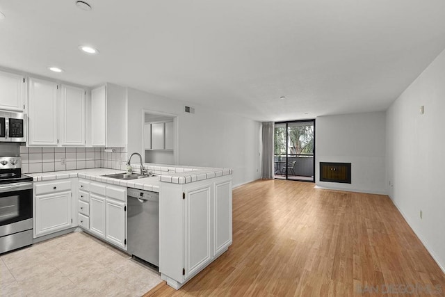 kitchen featuring backsplash, kitchen peninsula, sink, white cabinetry, and appliances with stainless steel finishes