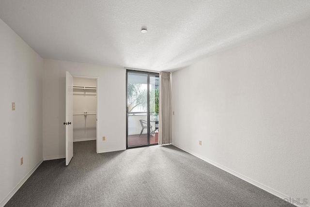 unfurnished bedroom with a wall of windows, access to outside, a closet, a textured ceiling, and a walk in closet