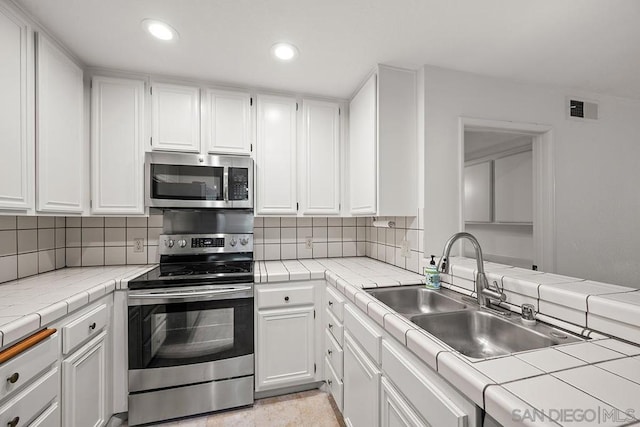 kitchen with white cabinets, appliances with stainless steel finishes, tile counters, tasteful backsplash, and sink