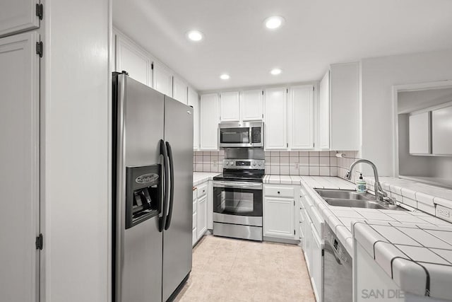 kitchen featuring tile counters, white cabinetry, stainless steel appliances, tasteful backsplash, and sink