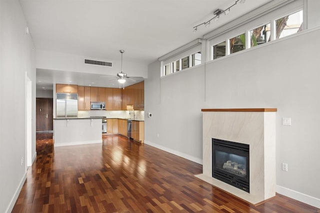 unfurnished living room featuring ceiling fan, a high end fireplace, dark hardwood / wood-style flooring, and track lighting