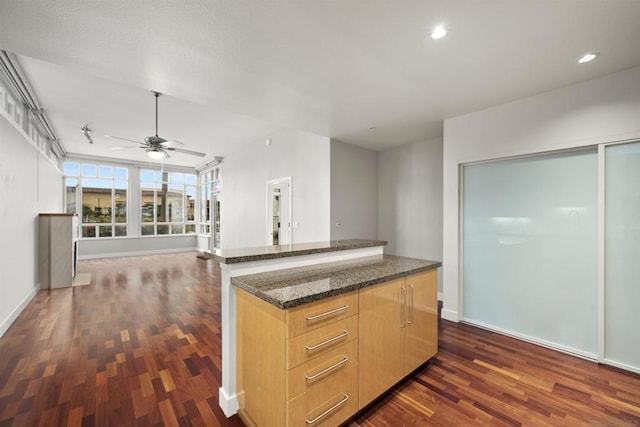 kitchen featuring a center island, dark wood-type flooring, light brown cabinets, dark stone countertops, and ceiling fan