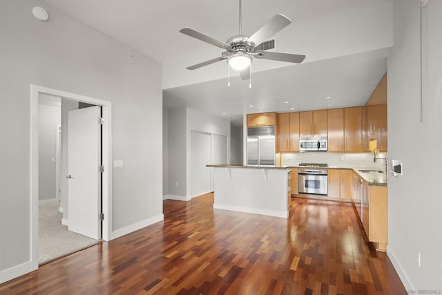 kitchen featuring appliances with stainless steel finishes, a center island, decorative backsplash, ceiling fan, and a breakfast bar area