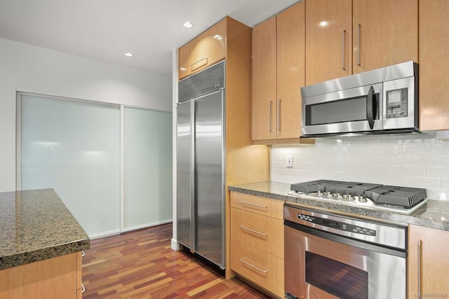 kitchen with tasteful backsplash, dark hardwood / wood-style flooring, dark stone counters, and stainless steel appliances