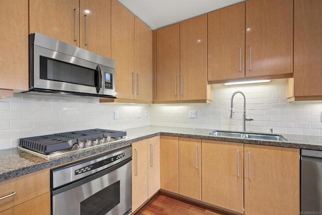 kitchen with appliances with stainless steel finishes, dark stone countertops, decorative backsplash, sink, and light wood-type flooring