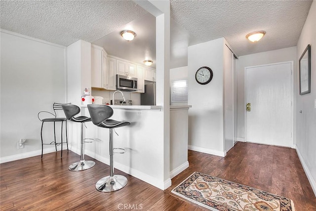 kitchen with dark hardwood / wood-style flooring, a kitchen breakfast bar, stainless steel appliances, and white cabinetry