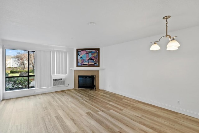 unfurnished living room with cooling unit, an inviting chandelier, a tiled fireplace, and light hardwood / wood-style floors