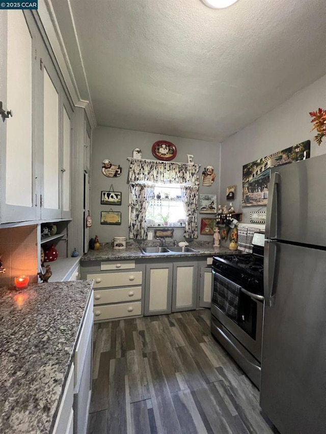 kitchen featuring a textured ceiling, dark wood-type flooring, stainless steel appliances, dark stone countertops, and sink