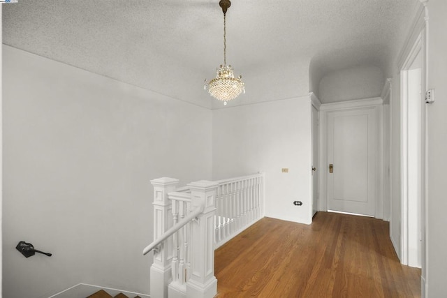 hallway featuring hardwood / wood-style flooring, a textured ceiling, and a notable chandelier