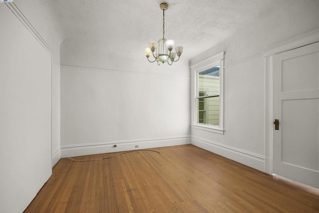 unfurnished dining area with a textured ceiling, an inviting chandelier, and hardwood / wood-style flooring