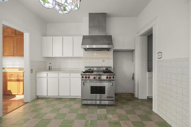 kitchen with a notable chandelier, stainless steel range, white cabinetry, and wall chimney exhaust hood