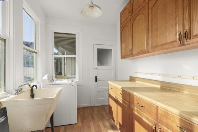 clothes washing area with light wood-type flooring, washing machine and dryer, cabinets, and sink