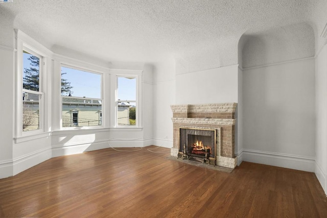 unfurnished living room with wood-type flooring, a brick fireplace, and a textured ceiling