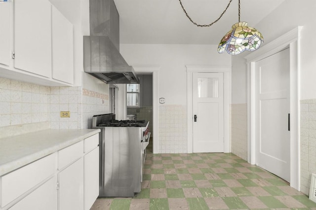 kitchen featuring island range hood, decorative light fixtures, gas stove, tile walls, and white cabinetry