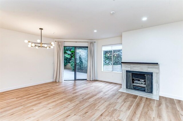 unfurnished living room with light hardwood / wood-style flooring, a notable chandelier, and a fireplace