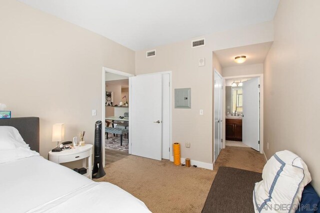 bedroom with ensuite bathroom, electric panel, and light colored carpet