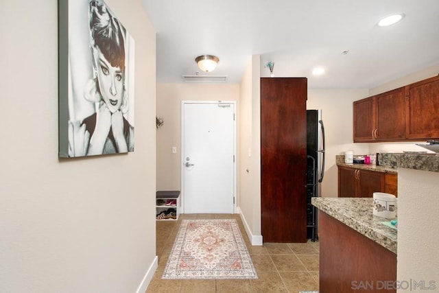 interior space featuring light tile patterned floors, light stone countertops, and black fridge