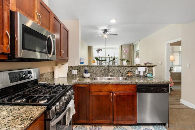 kitchen featuring kitchen peninsula, ceiling fan, appliances with stainless steel finishes, light stone countertops, and sink