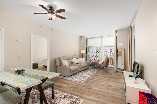 living room featuring ceiling fan, a wall of windows, and light hardwood / wood-style floors