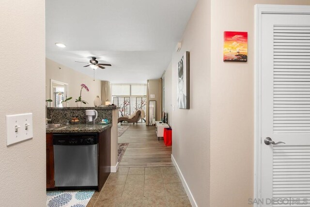 kitchen featuring ceiling fan, light tile patterned floors, stainless steel dishwasher, and dark stone countertops