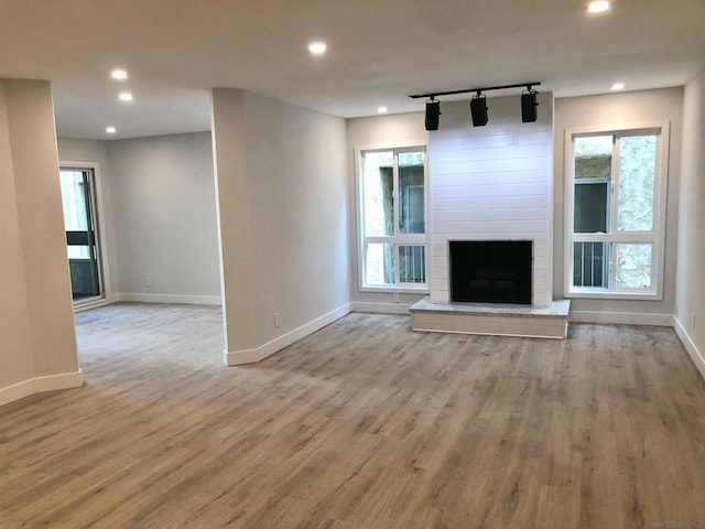 unfurnished living room featuring light wood-type flooring, rail lighting, a fireplace, and plenty of natural light