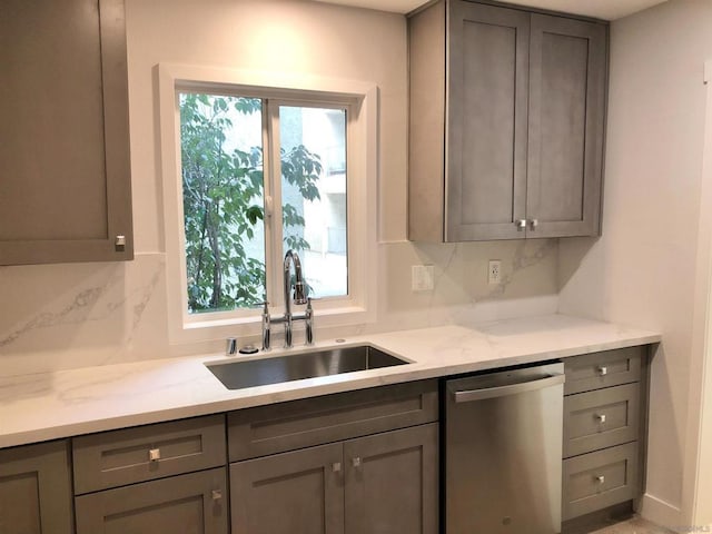 kitchen featuring light stone countertops, gray cabinetry, stainless steel dishwasher, and sink