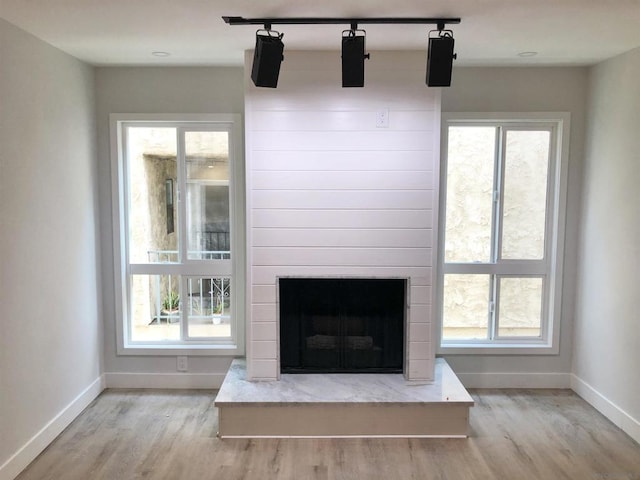 unfurnished living room with light wood-type flooring, a large fireplace, and rail lighting