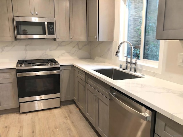 kitchen featuring light stone countertops, stainless steel appliances, decorative backsplash, sink, and light wood-type flooring