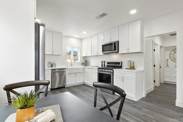 kitchen with dark wood-type flooring, backsplash, white cabinets, and stainless steel appliances