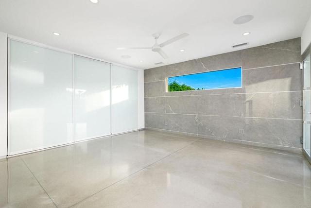 unfurnished room featuring ceiling fan and tile walls