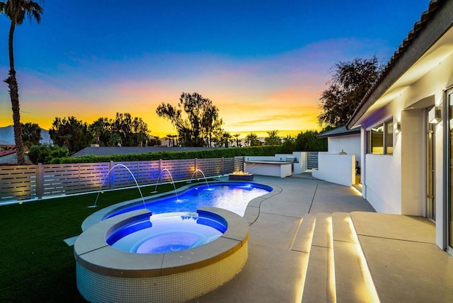 pool at dusk with pool water feature, an in ground hot tub, and a patio