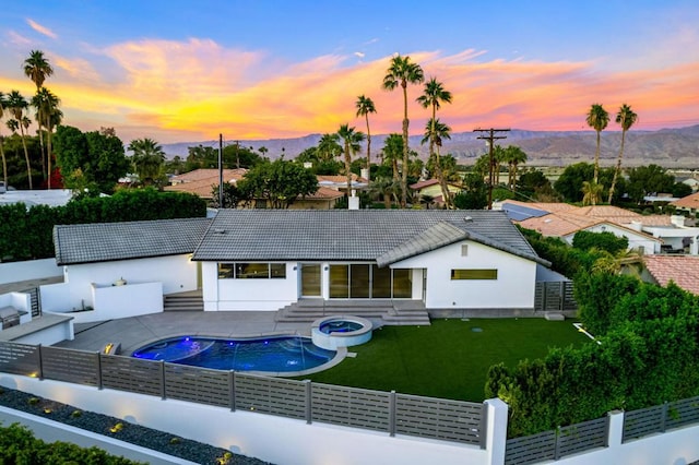 back house at dusk with a mountain view, a fenced in pool, a lawn, and a patio