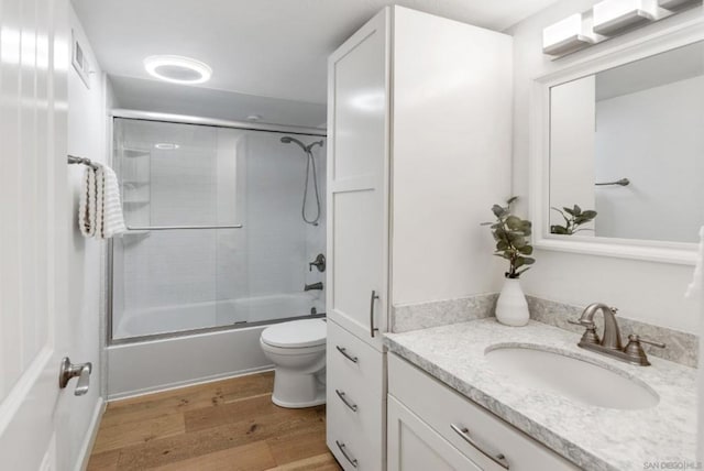 full bathroom featuring toilet, enclosed tub / shower combo, wood-type flooring, and vanity