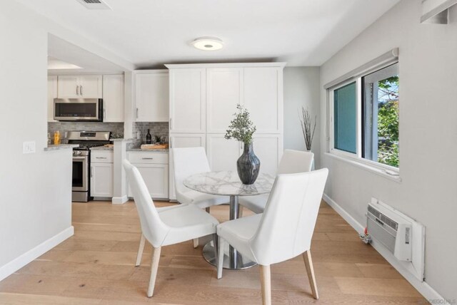 dining room with an AC wall unit and light hardwood / wood-style floors