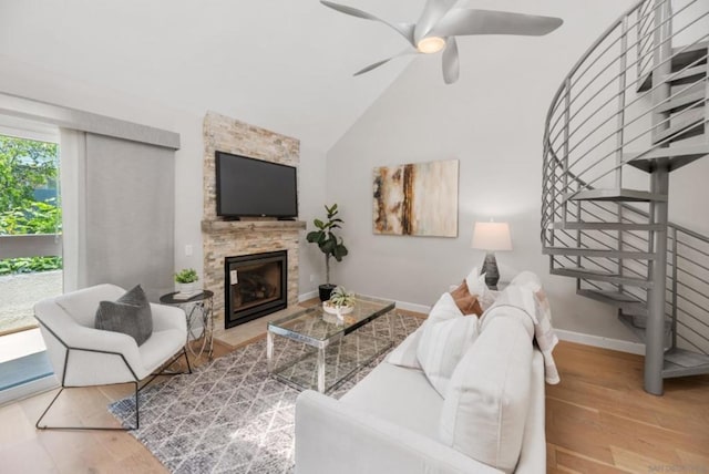 living room featuring vaulted ceiling, ceiling fan, wood-type flooring, and a stone fireplace