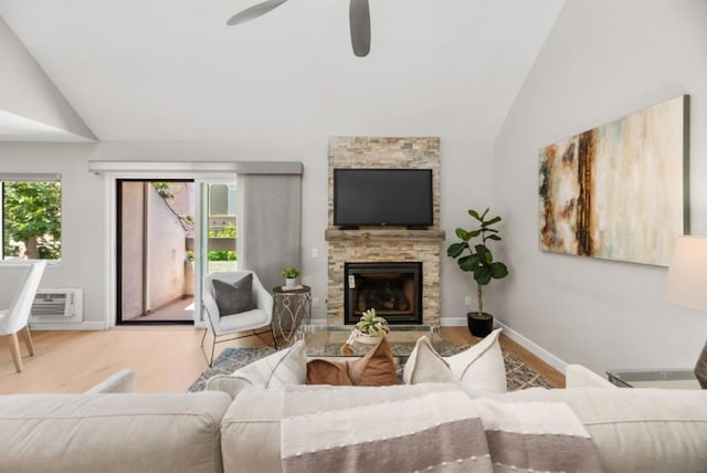 living room featuring lofted ceiling, hardwood / wood-style flooring, a stone fireplace, and a wall unit AC