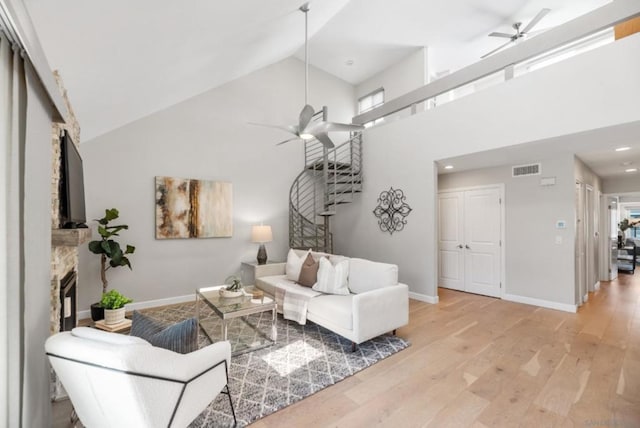 living room with high vaulted ceiling, a healthy amount of sunlight, a stone fireplace, and light hardwood / wood-style floors