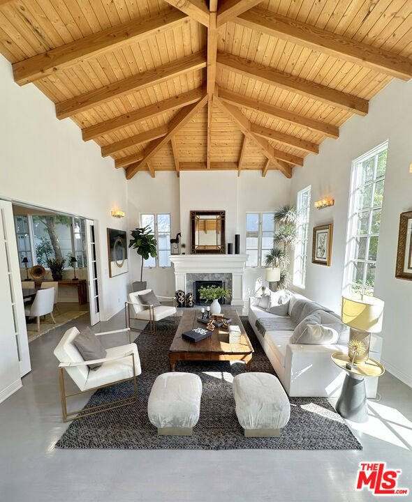 living room featuring wood ceiling, high vaulted ceiling, concrete flooring, a fireplace, and beamed ceiling