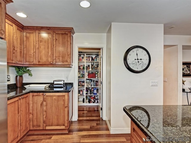 kitchen with hardwood / wood-style flooring, stainless steel fridge, and dark stone countertops