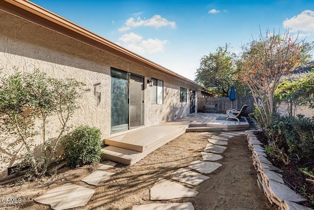 exterior space featuring fence, a wooden deck, and stucco siding