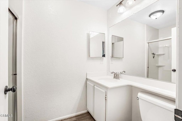 bathroom with a shower with door, toilet, vanity, wood finished floors, and baseboards